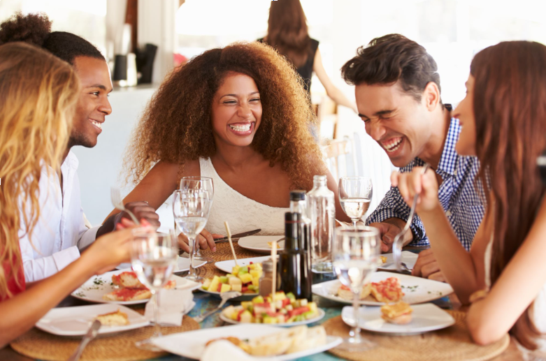 A diverse group of friends laughing, talking, and enjoying a meal together at a restaurant table in Fairfield, Connecticut.