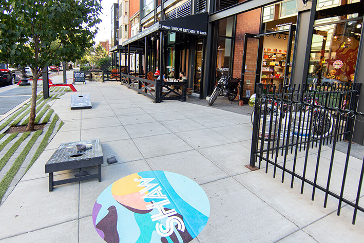 A tree-lined sidewalk in Shaw, Washington, DC with local shops and a Shaw street mural
