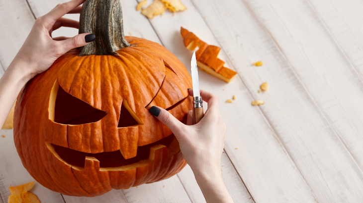 Slender hands with painted nails remove a cutout of pumpkin from a jack-o-lantern