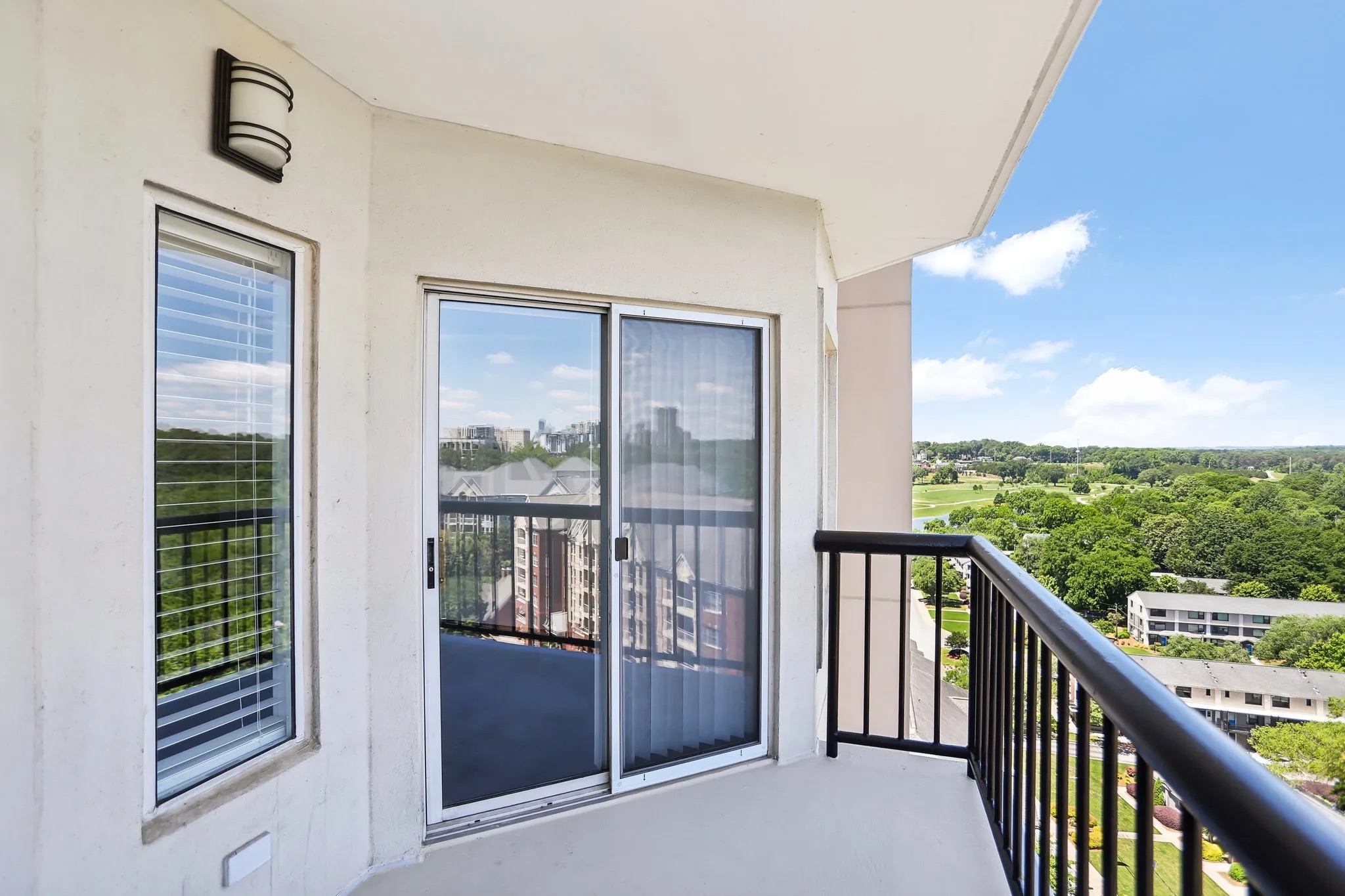 A concrete balcony featuring black railings and a sliding glass door overlooking brick buildings at Colonial Homes.