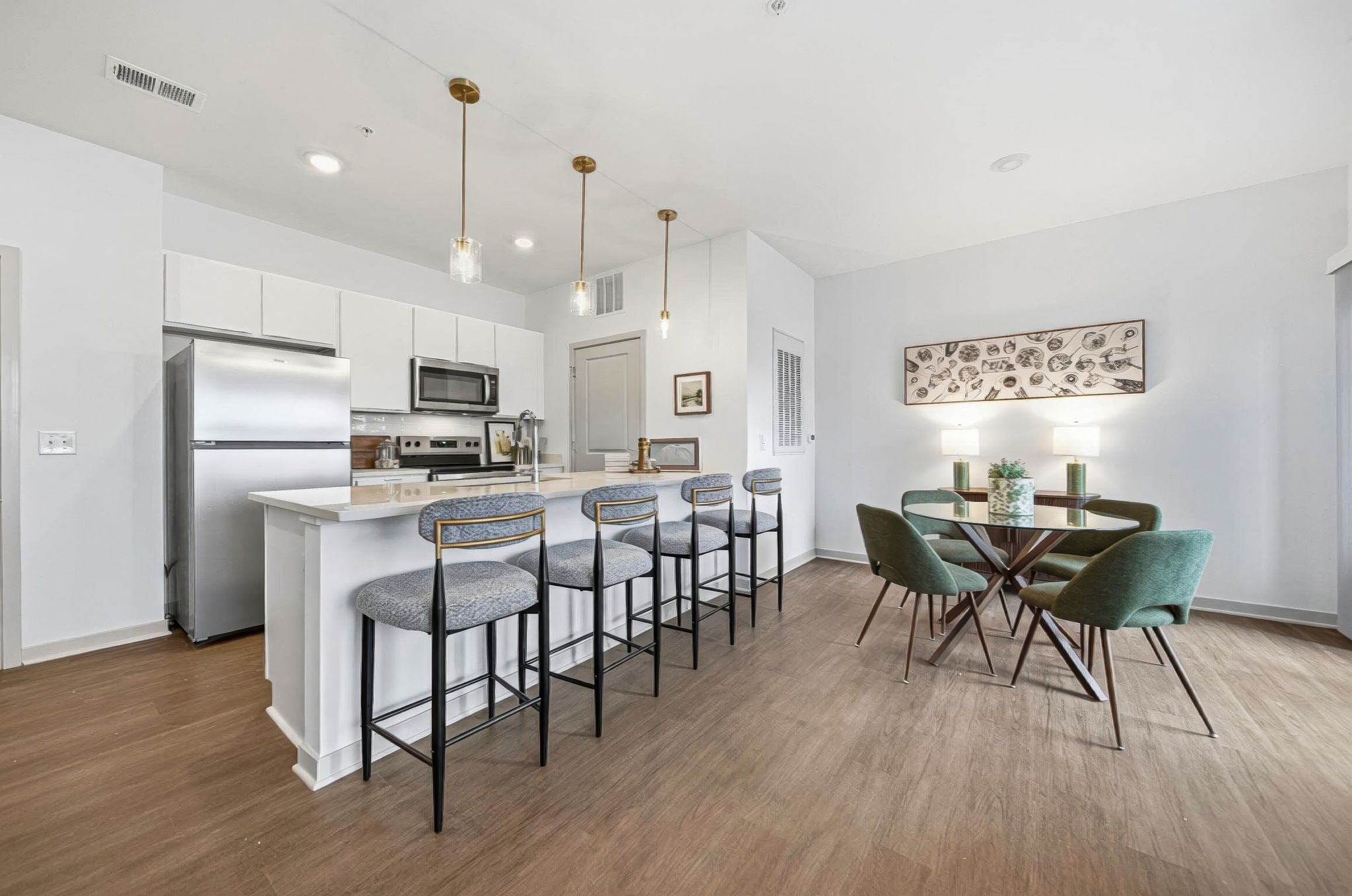 Modern apartment kitchen and dining area at Lawrence Square Apartments in Columbus, Ohio, featuring quartz countertops, stainless steel appliances, white cabinetry, pendant lighting, and luxury vinyl plank flooring.