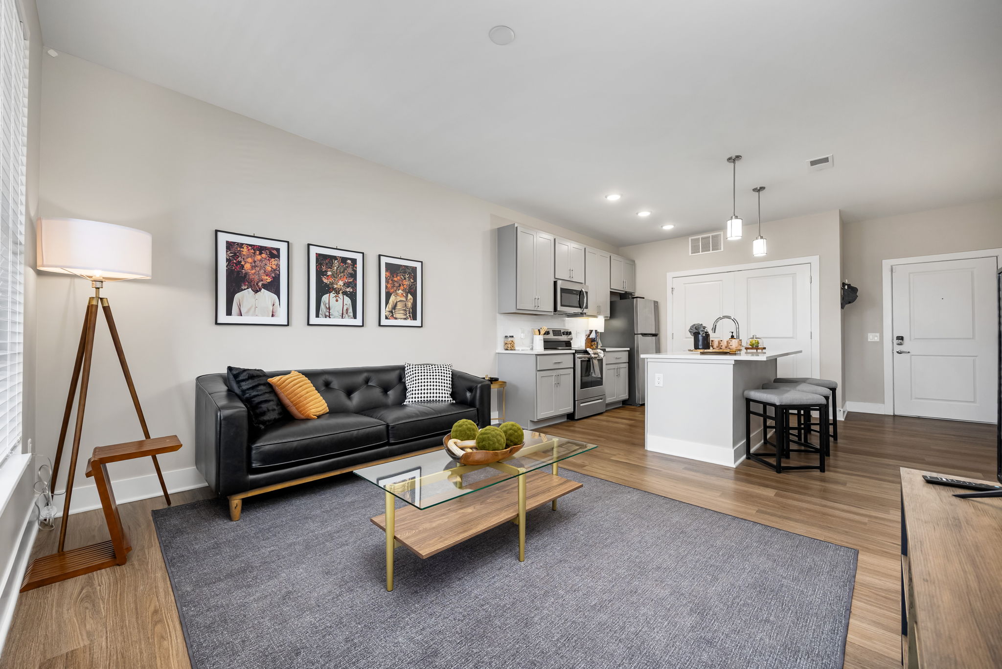 Modern living room and kitchen interior at Residences at Topiary Park, featuring stainless steel appliances, gray cabinetry, hardwood-style floors, and contemporary décor.