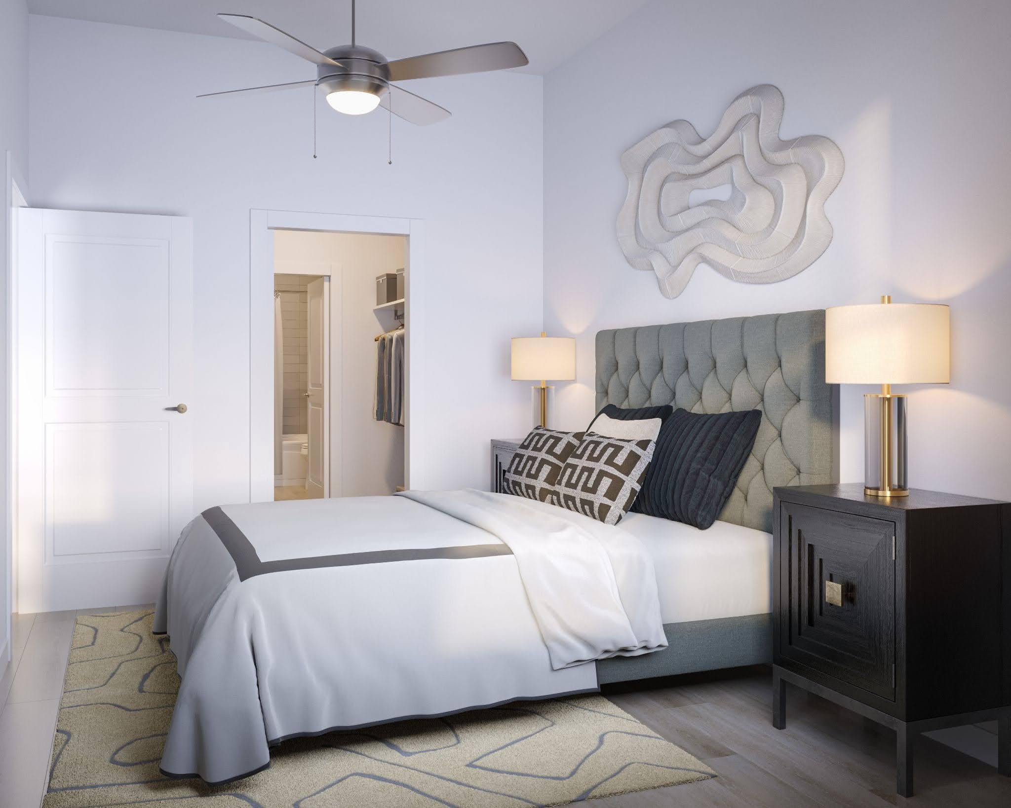 Furnished bedroom at SOFI at 6311 with a tufted gray upholstered headboard, matching nightstands and lamps, patterned area rug, and a ceiling fan