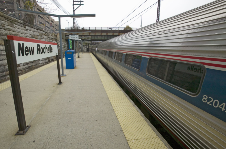 Amtrak train alongside New Rochelle station platform with station sign