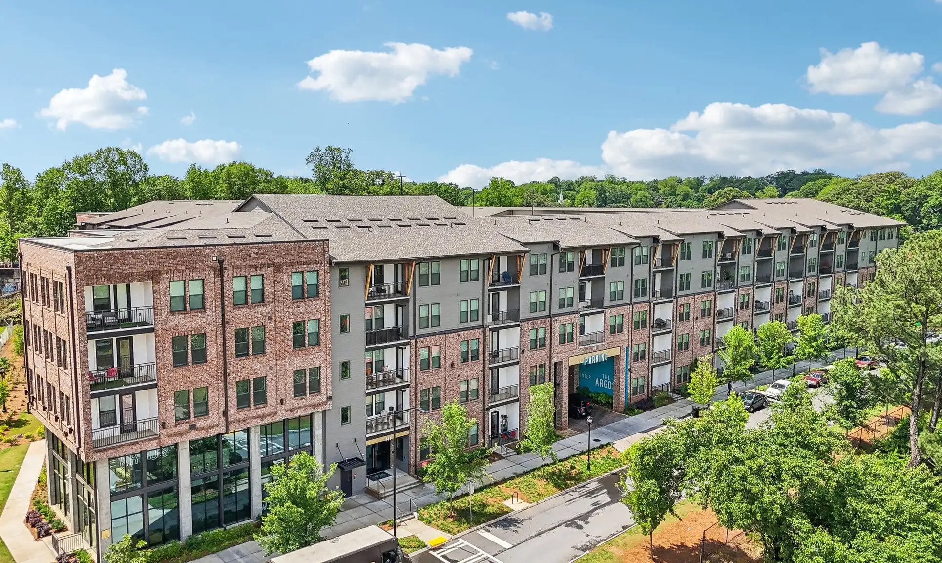 Aerial view of The Argos Apartments at Grant Park featuring modern mid-rise apartments with brick and gray facades, balconies, and lush surrounding trees.