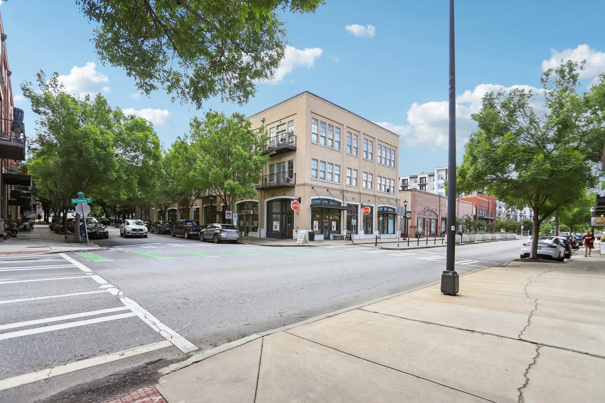 A tan building standing on a street corner featuring white crosswalk lines and green trees growing along the sidewalks.