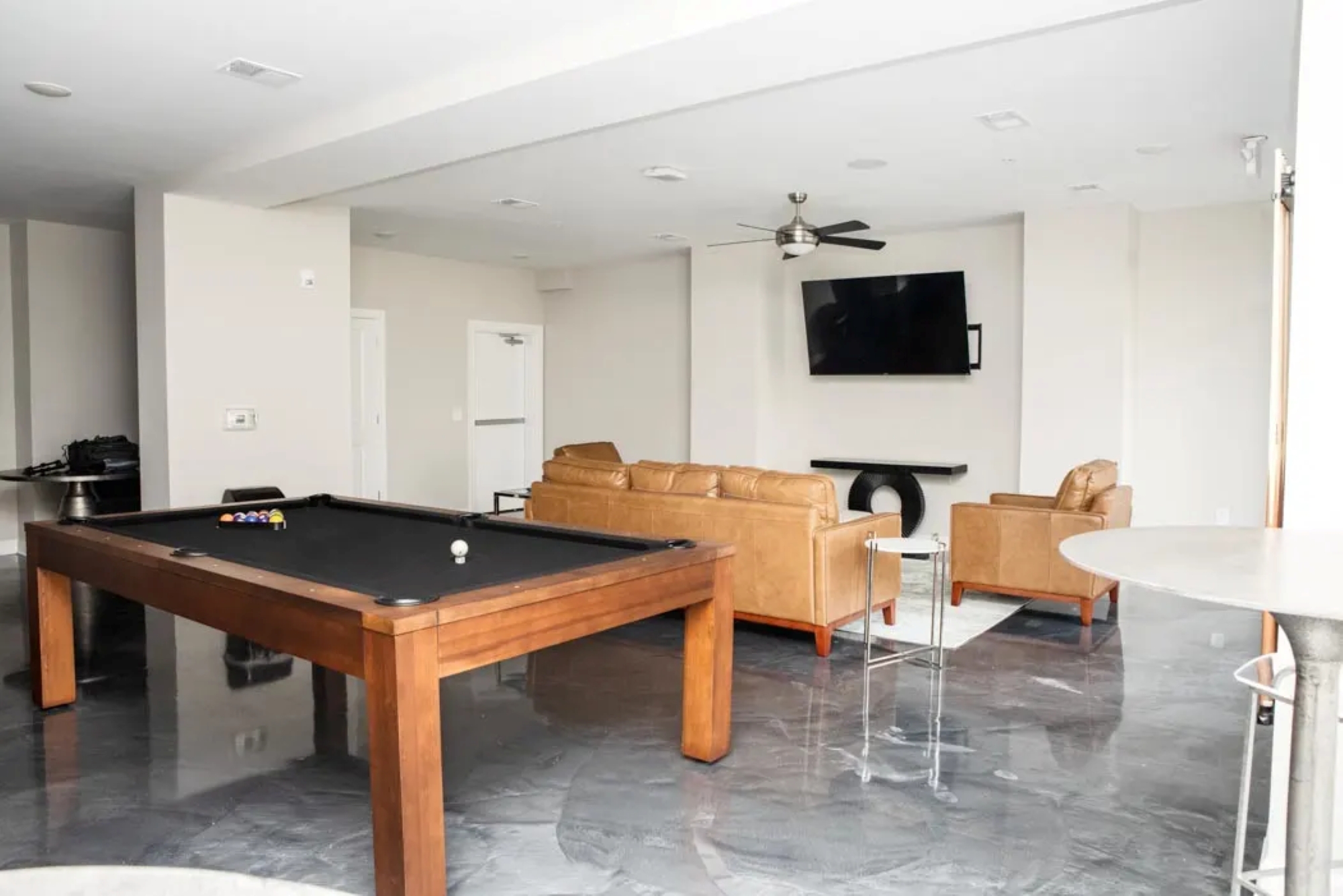 A resident clubhouse lounge featuring a wooden pool table, tan leather seating, and a wall-mounted television.