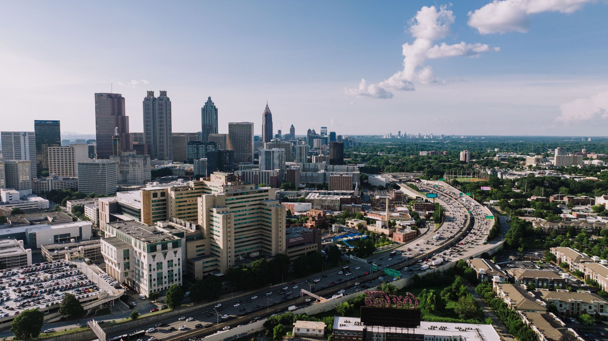 An aerial view showing tall skyscrapers standing near large multi-story buildings and a curved highway filled with cars.
