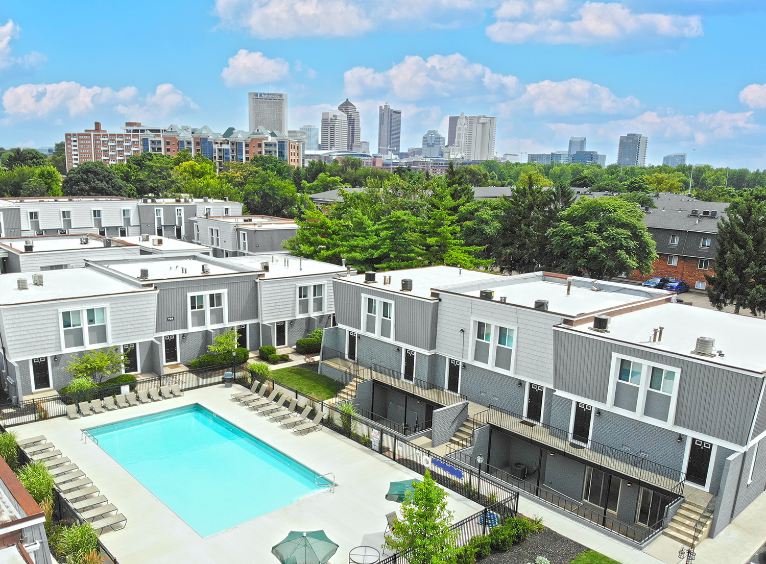 Aerial view of Sonnenblick townhome community in Columbus, Ohio, featuring a central outdoor pool, modern gray exteriors, landscaped grounds, and skyline views of downtown Columbus.