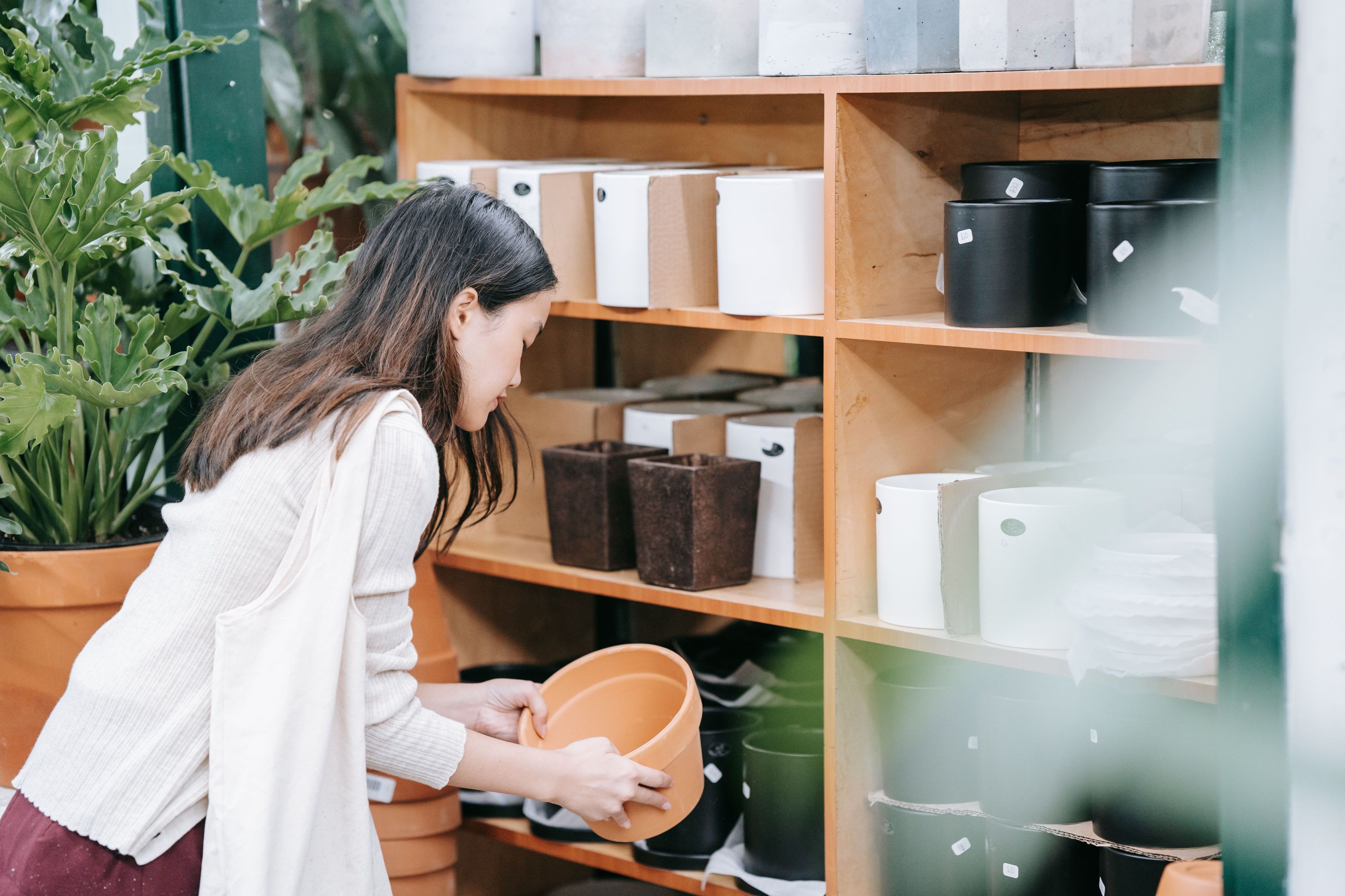 A woman picking out a terracotta plant pot while browsing wooden shelves filled with ceramic planters in a shop.