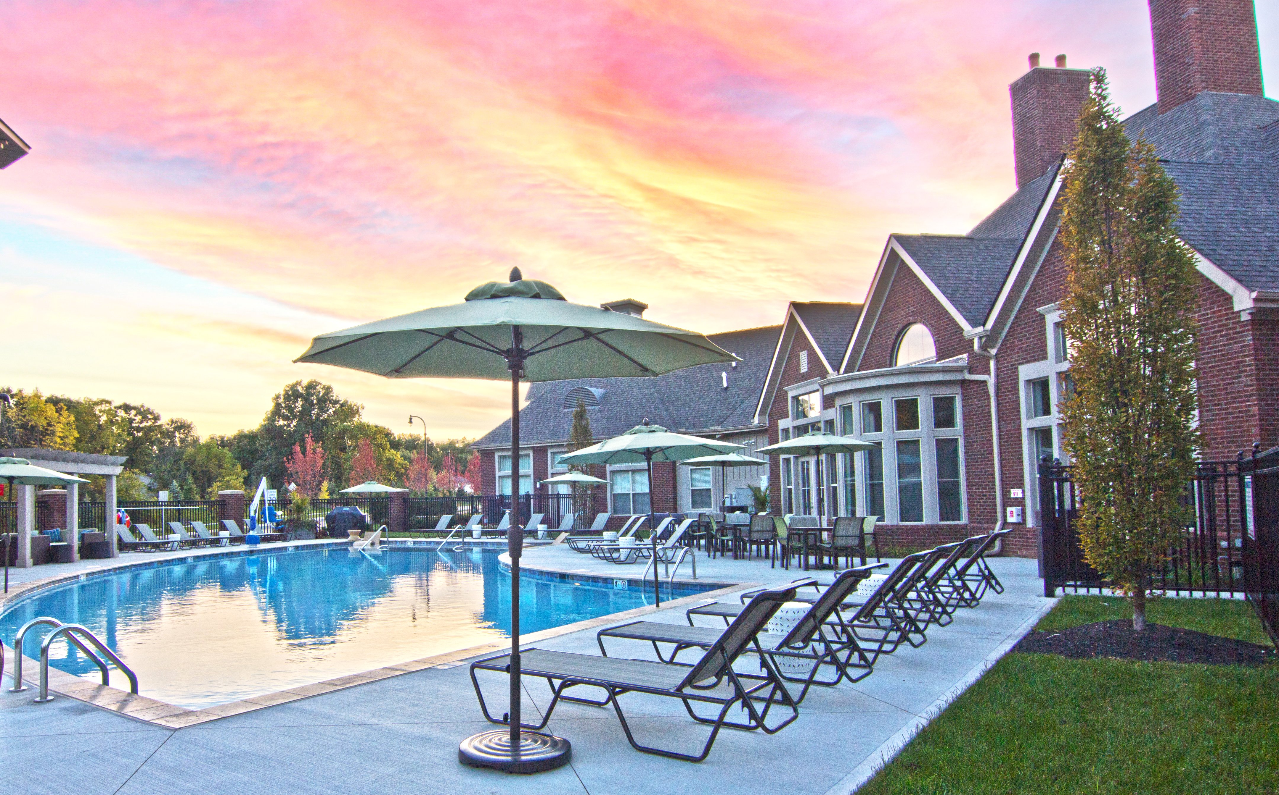 Resort-style pool at The Ravines at Westar featuring lounge chairs, umbrellas, and clubhouse at sunset.