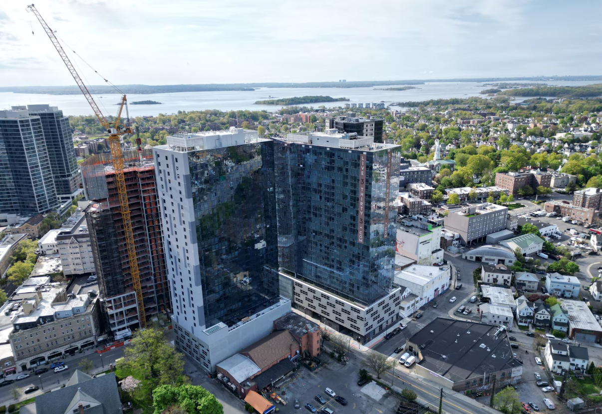 Aerial view of Encore Apartments in New Rochelle featuring a modern high-rise building, surrounding neighborhood, and Long Island Sound in the background