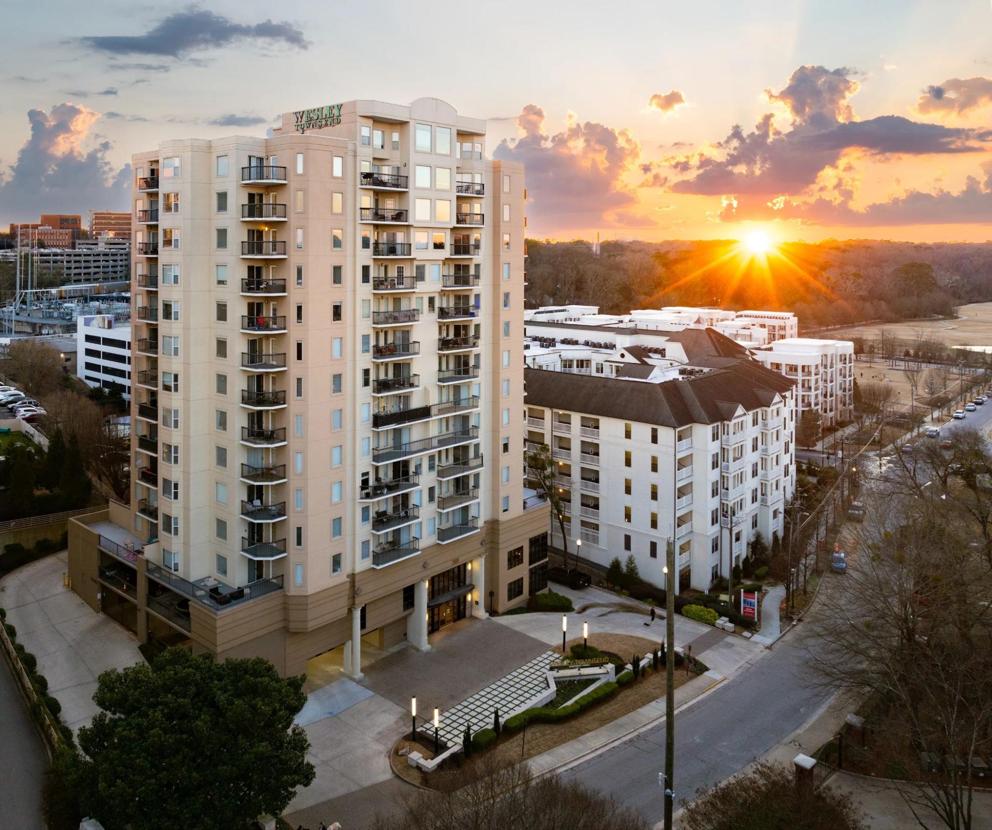 The tall Wesley Townsend apartment building standing near a paved street and other buildings under a bright sunset sky.
