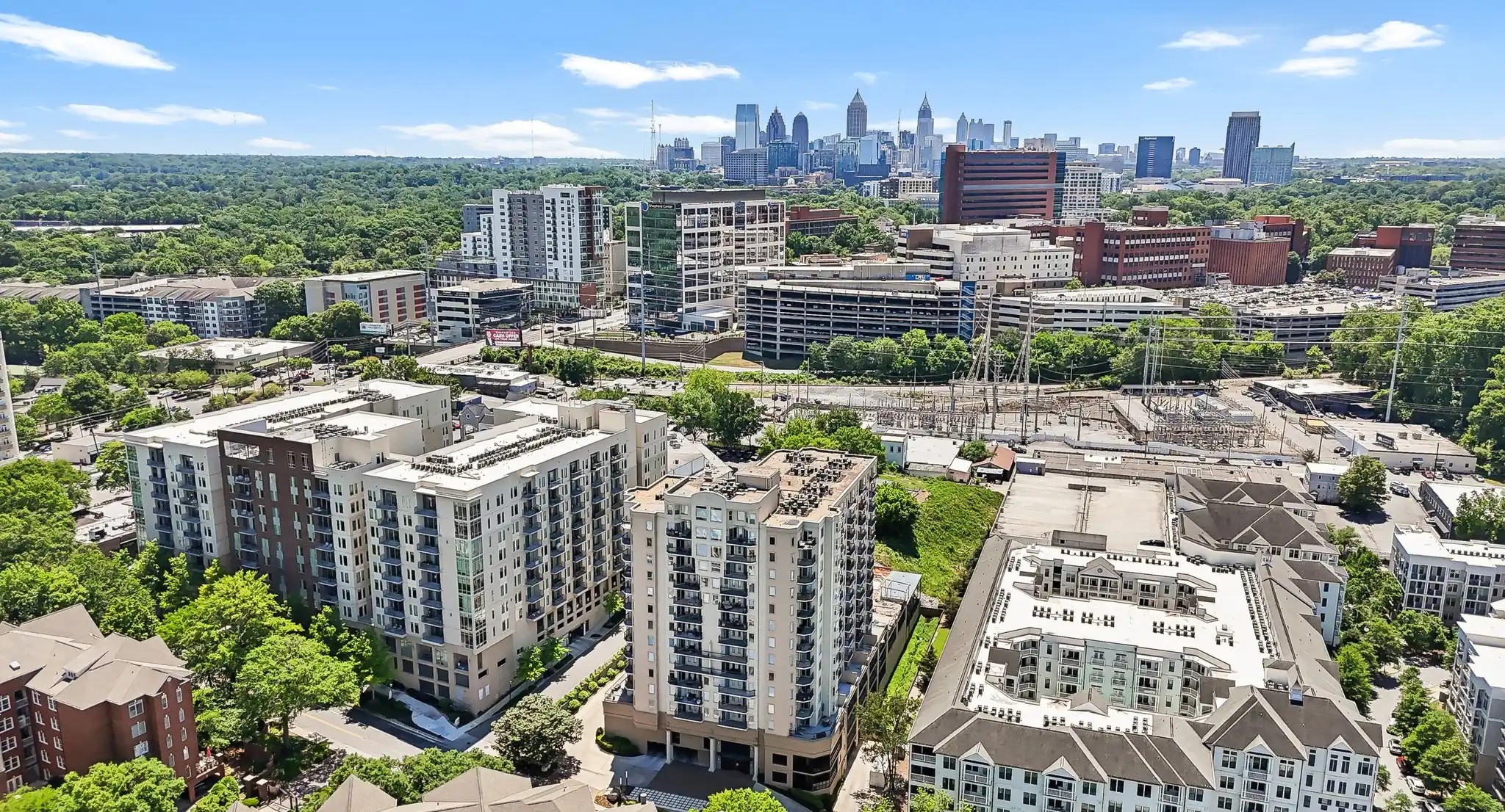 Large apartment buildings standing near green trees and a power station overlooking a city skyline at Colonial Homes.