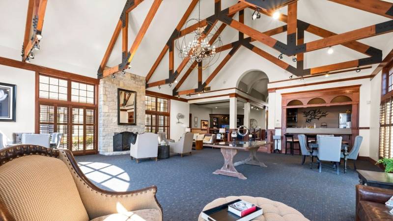 Elegant clubhouse interior at Asherton of Dublin Apartments featuring vaulted wood-beam ceilings, a stone fireplace, and comfortable seating areas.