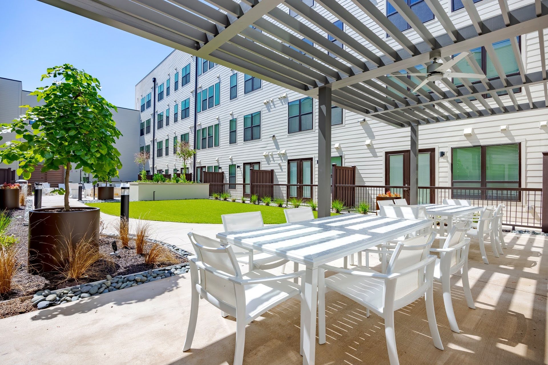 Shaded pergola with white outdoor dining tables and chairs beside the landscaped courtyard lawn at SOFI at 6311