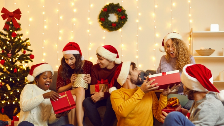 smiling young adults gather on a couch exchanging gifts