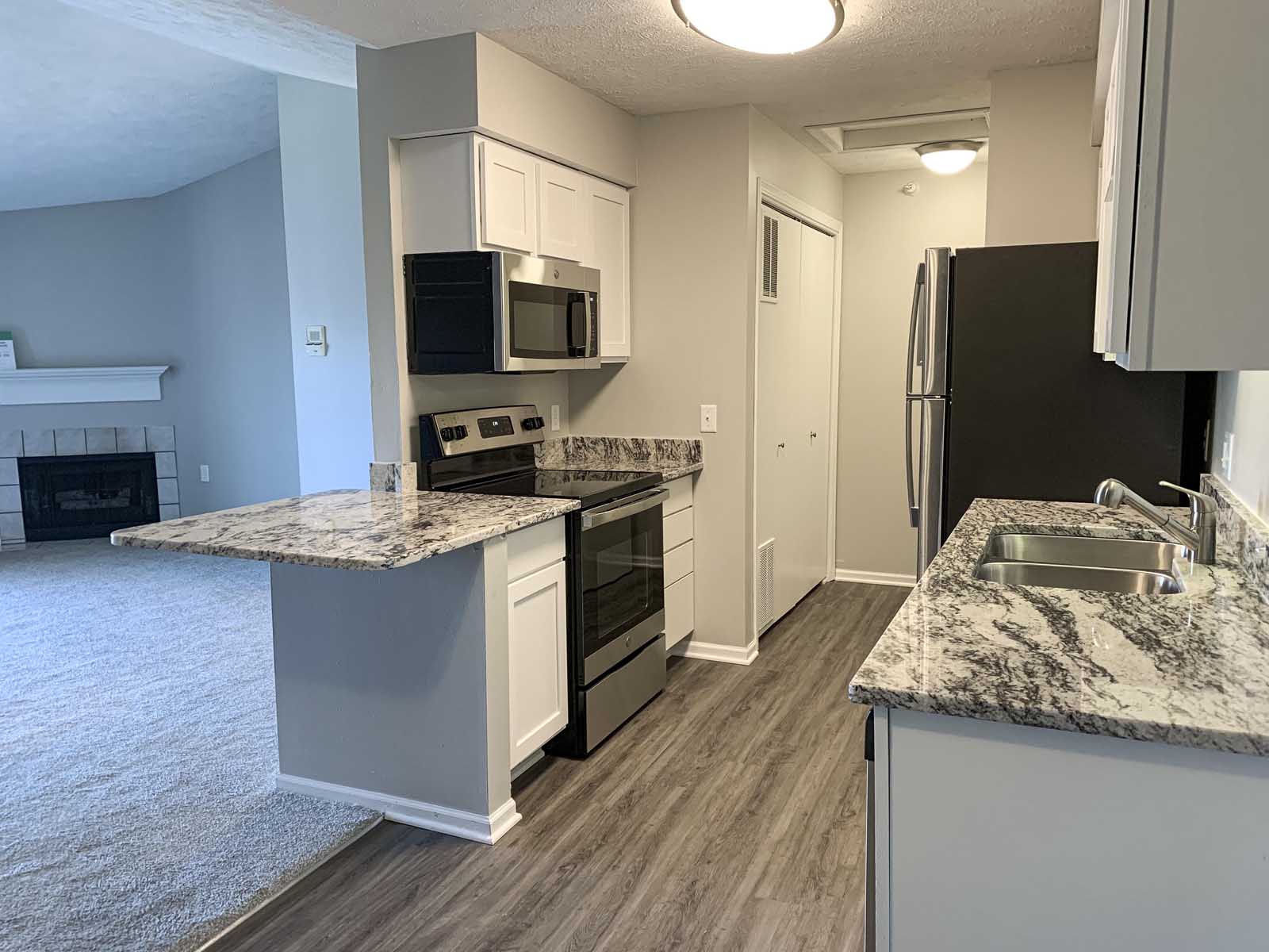 A kitchen with a breakfast bar, granite countertops, stainless steel appliances, and white wooden cabinets.