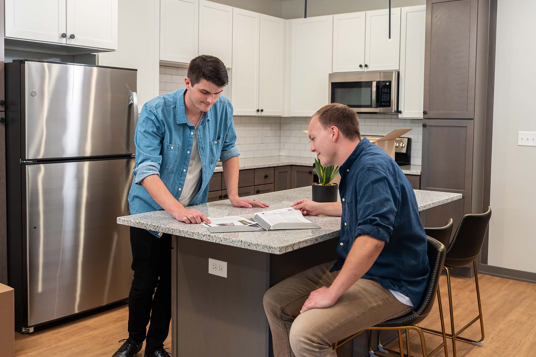 two men sitting at a kitchen counter looking at a move-in folder