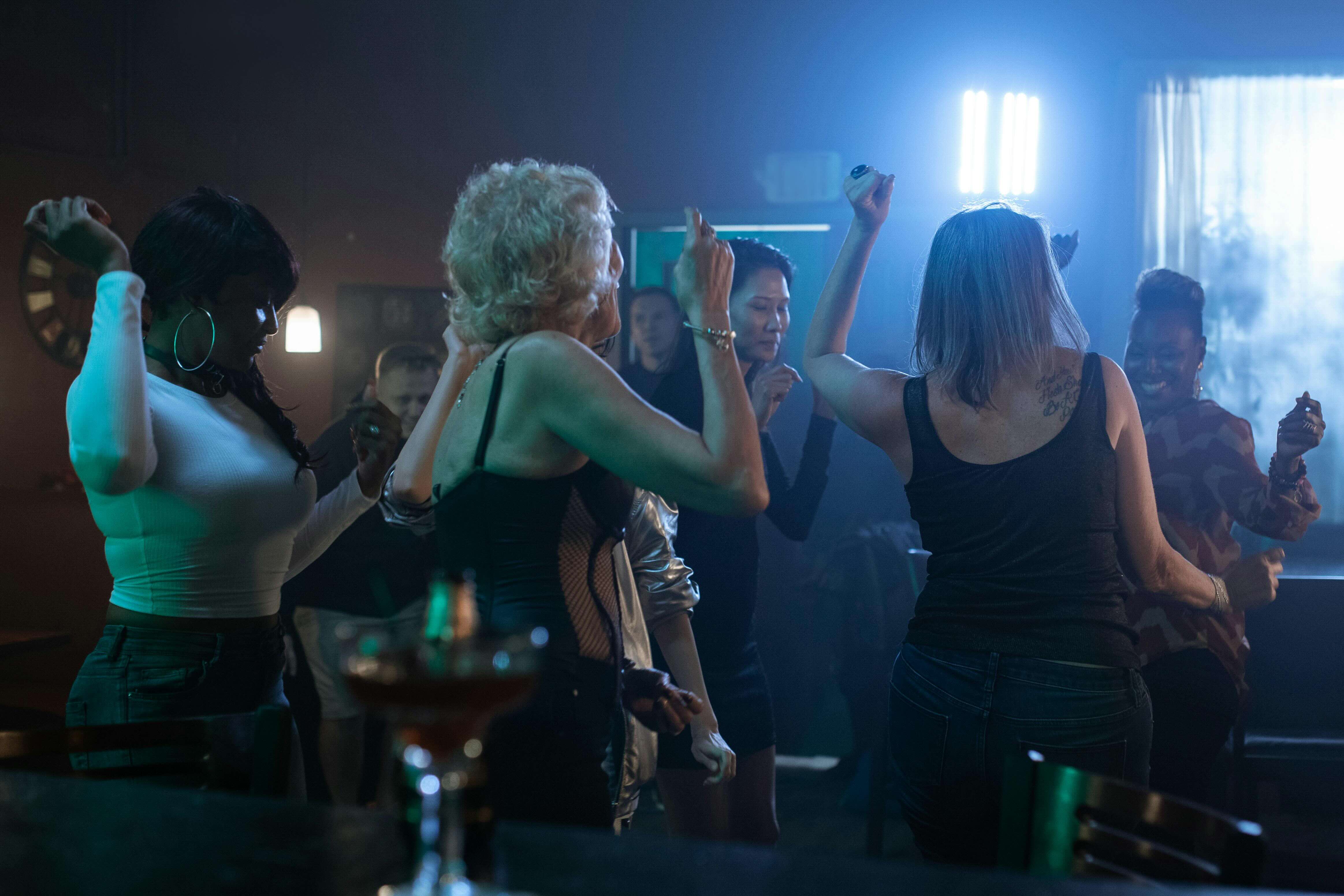 A group of women wearing casual clothing dancing together under bright blue lighting inside a dark nightclub.