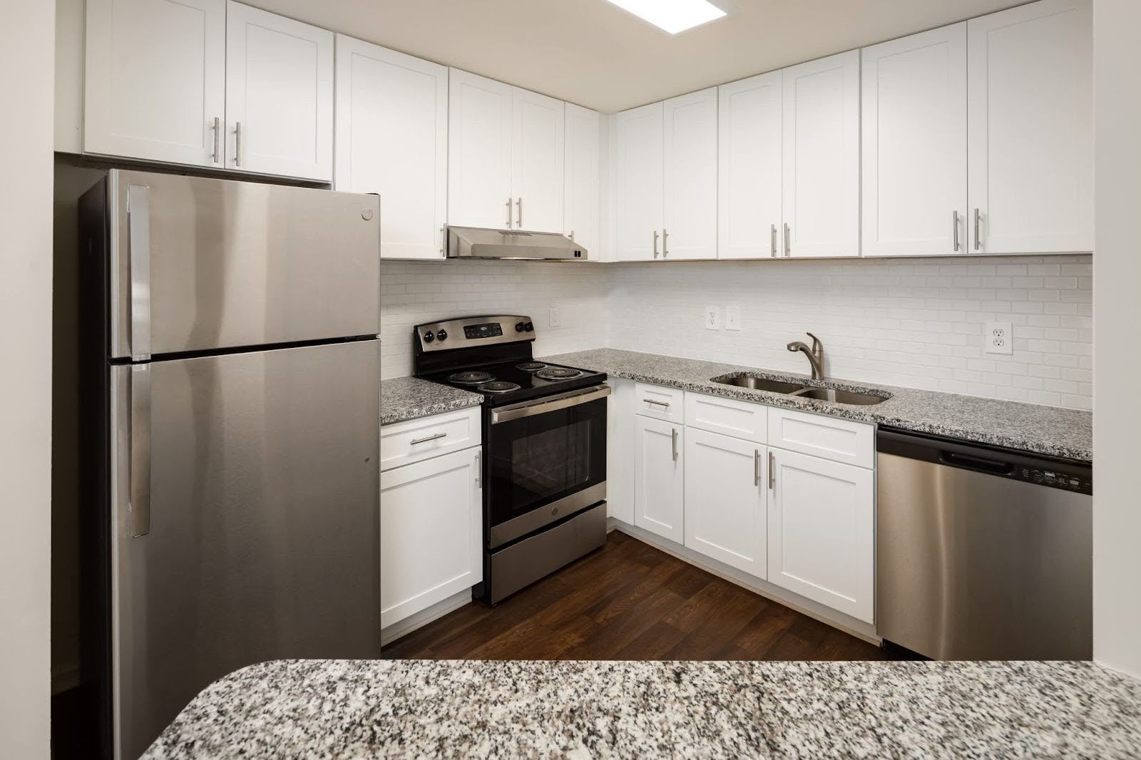Modern Wesley Hampstead Apartments kitchen with white shaker cabinets, stainless steel appliances, subway tile backsplash, and granite countertops.