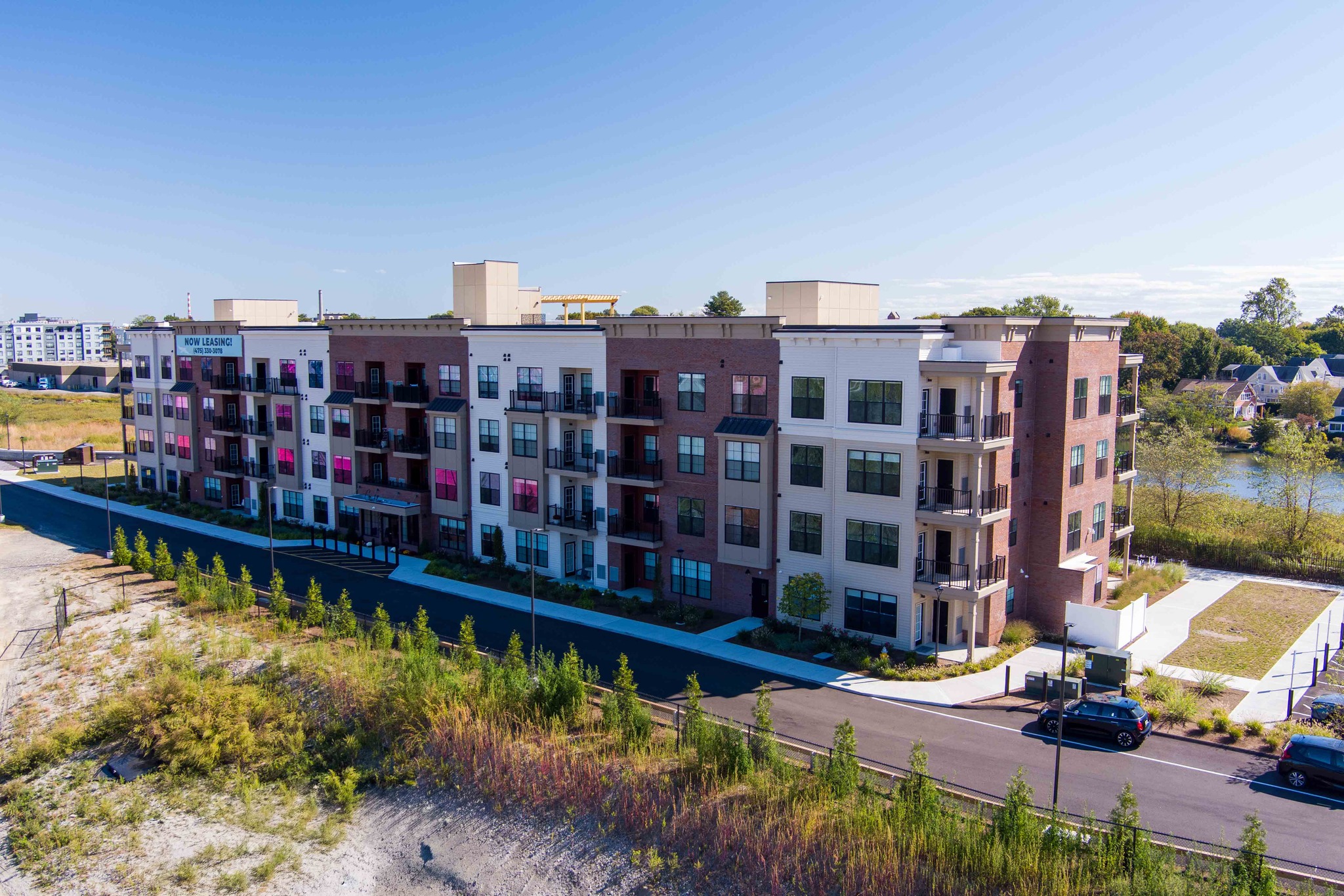 Aerial view of the modern, multi-story apartment building at Creekline Apartments, featuring balconies and brick accents, situated near a body of water.