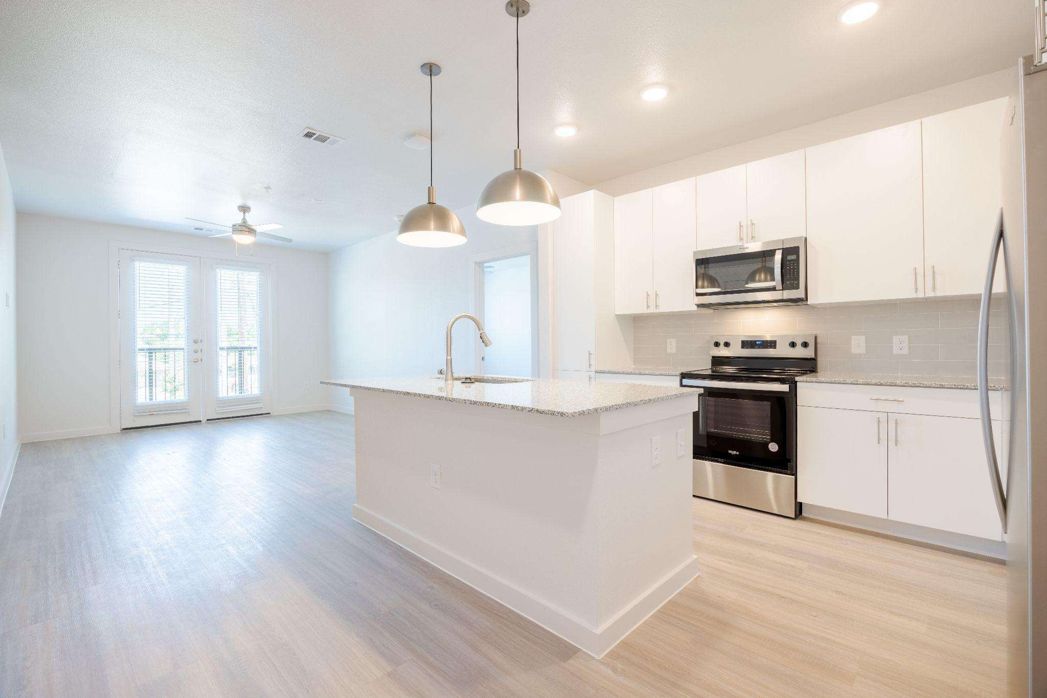 Open-concept kitchen with white cabinetry, stainless steel appliances, and an island, opening onto a living area at SOFI at 6311