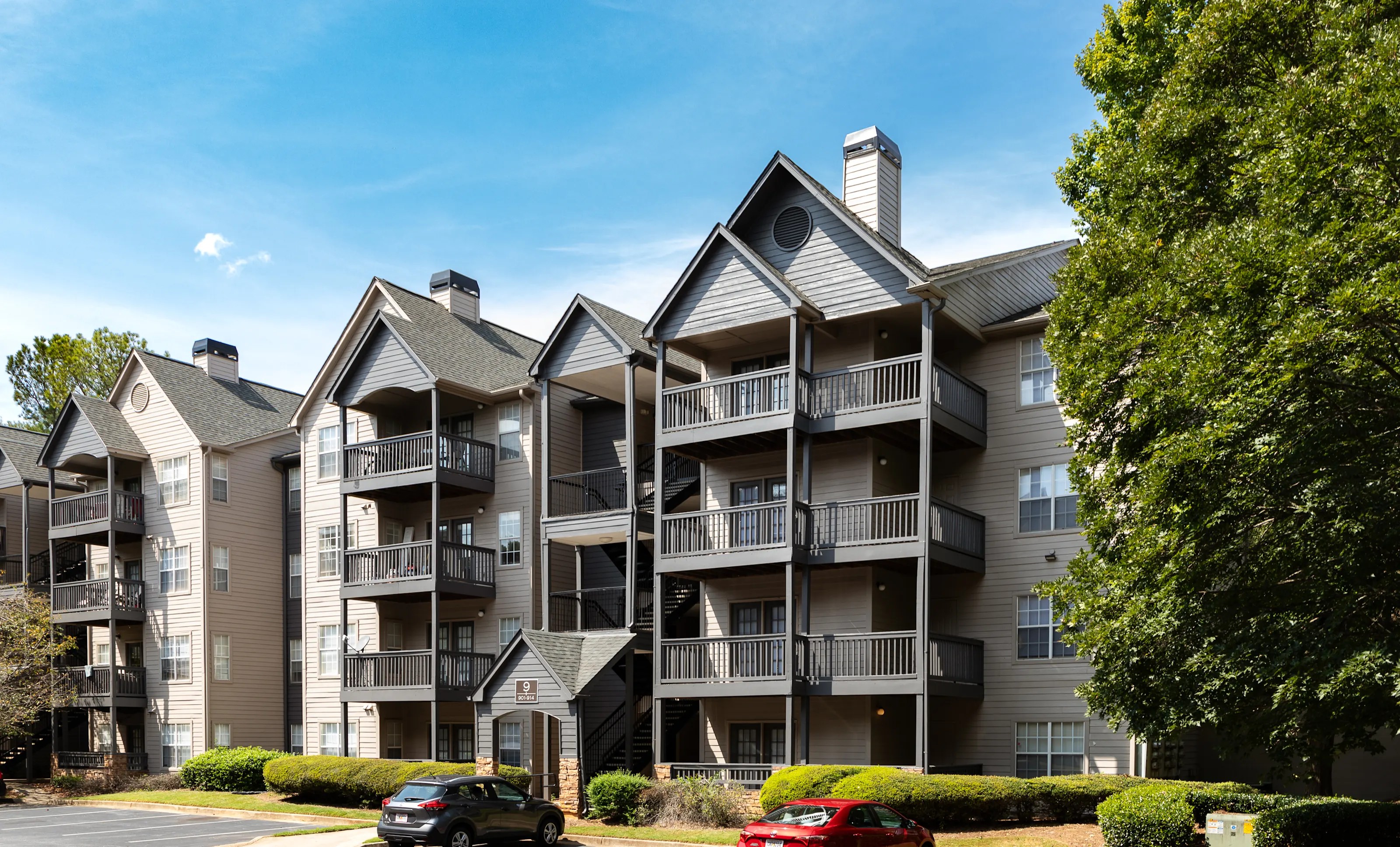The Wesley Hampstead Apartments building featuring dark balconies standing near a parking lot and green trees.
