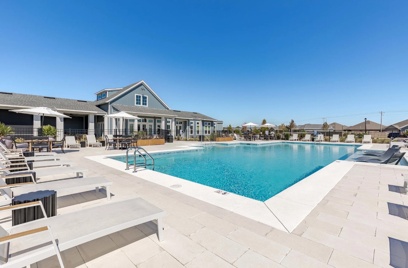 Large resort-style swimming pool with lounge chairs, umbrellas, and a blue clubhouse building at Outpost Orchard in Foley, AL.