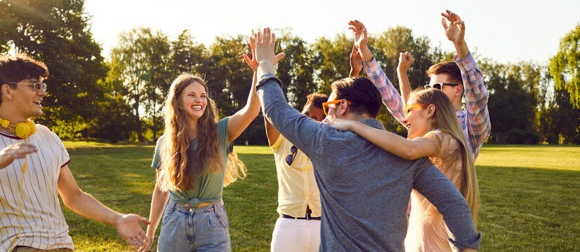 A diverse group of young adults in Atlanta, GA, celebrating outdoors in a park, laughing and giving high-fives with their arms raised.