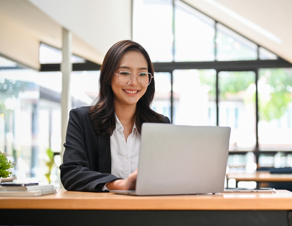 Woman working on a laptop at a bright coworking space in New Rochelle with large windows and natural light.