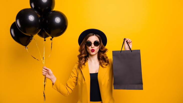 woman in black and yellow outfit holding black balloons and a black shopping bag