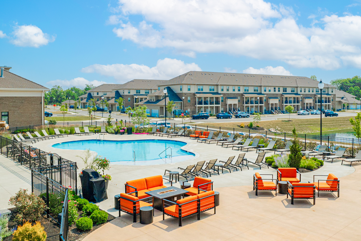 Resort-style outdoor pool area at Beulah Place in Grove City, Ohio, featuring lounge chairs, bright orange seating, landscaped surroundings, and townhome buildings in the background.