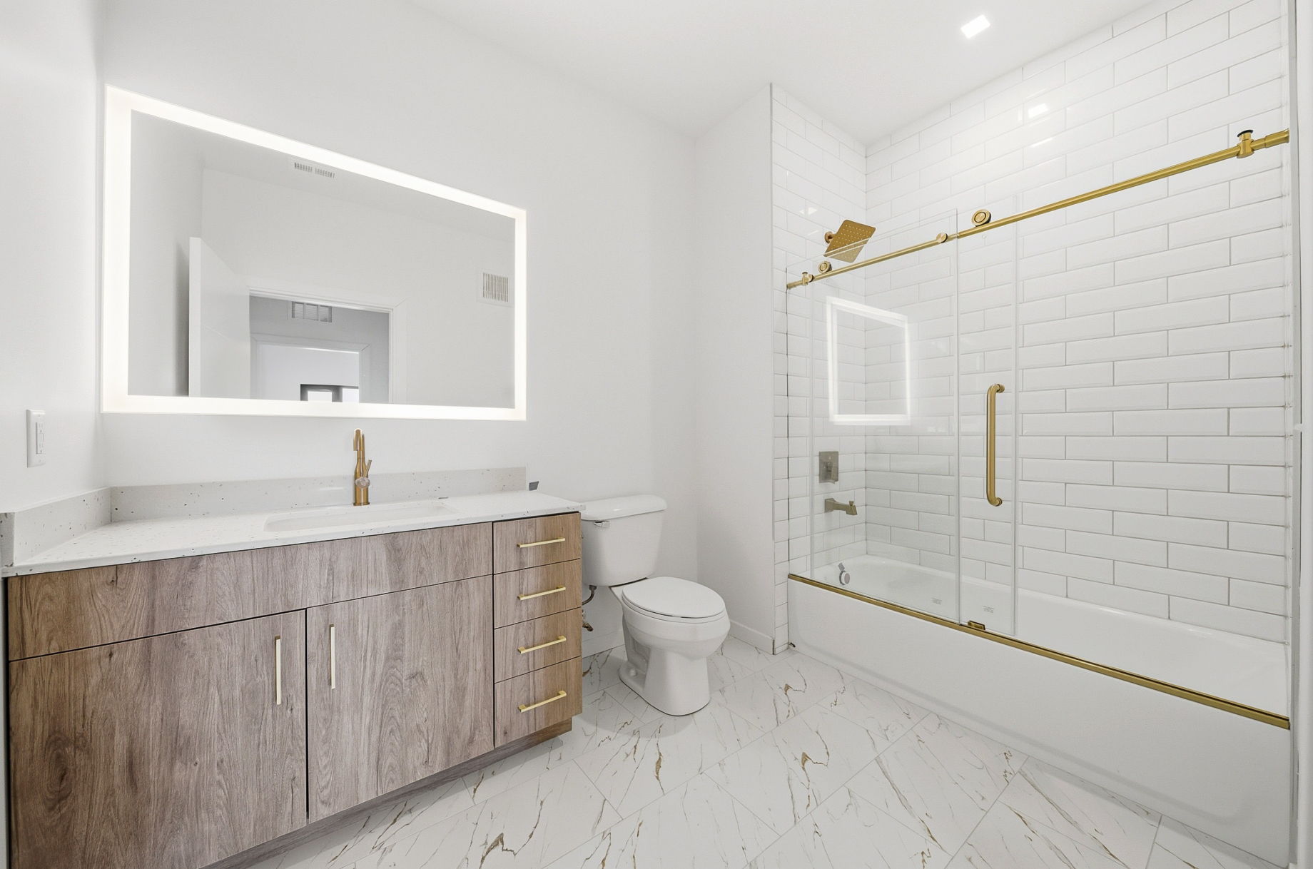 Modern bathroom at Webster Station Flats featuring a walk-in tiled shower, LED mirrors, wood vanity, and bronze fixtures.