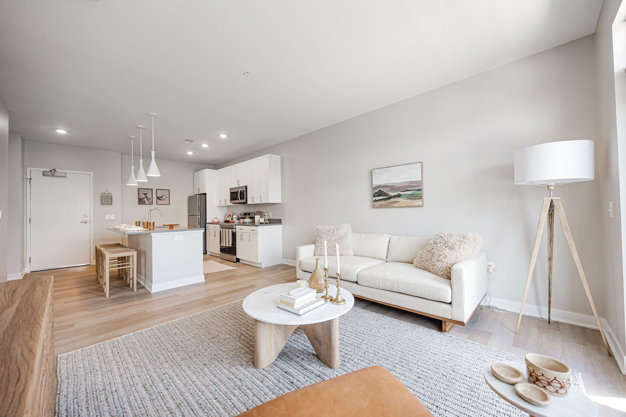 Open-concept apartment interior at Westrich in Franklinton, Ohio, featuring luxury vinyl plank flooring, stainless steel appliances, modern white cabinetry, pendant lighting, and a spacious living area.