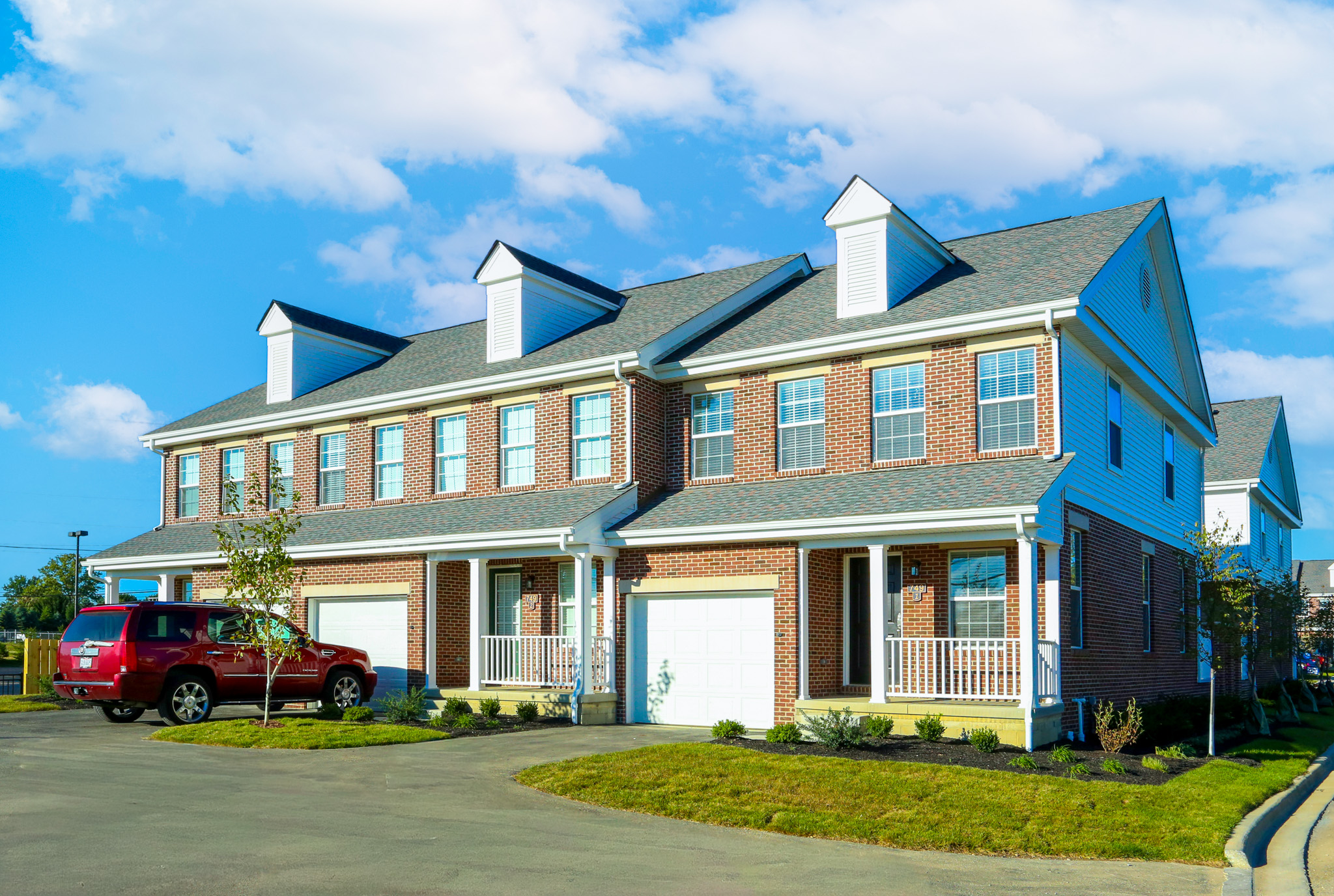 Brick townhome exterior at Enclave Village in Lewis Center, Ohio, featuring private porches, attached garages, and a well-maintained residential setting.