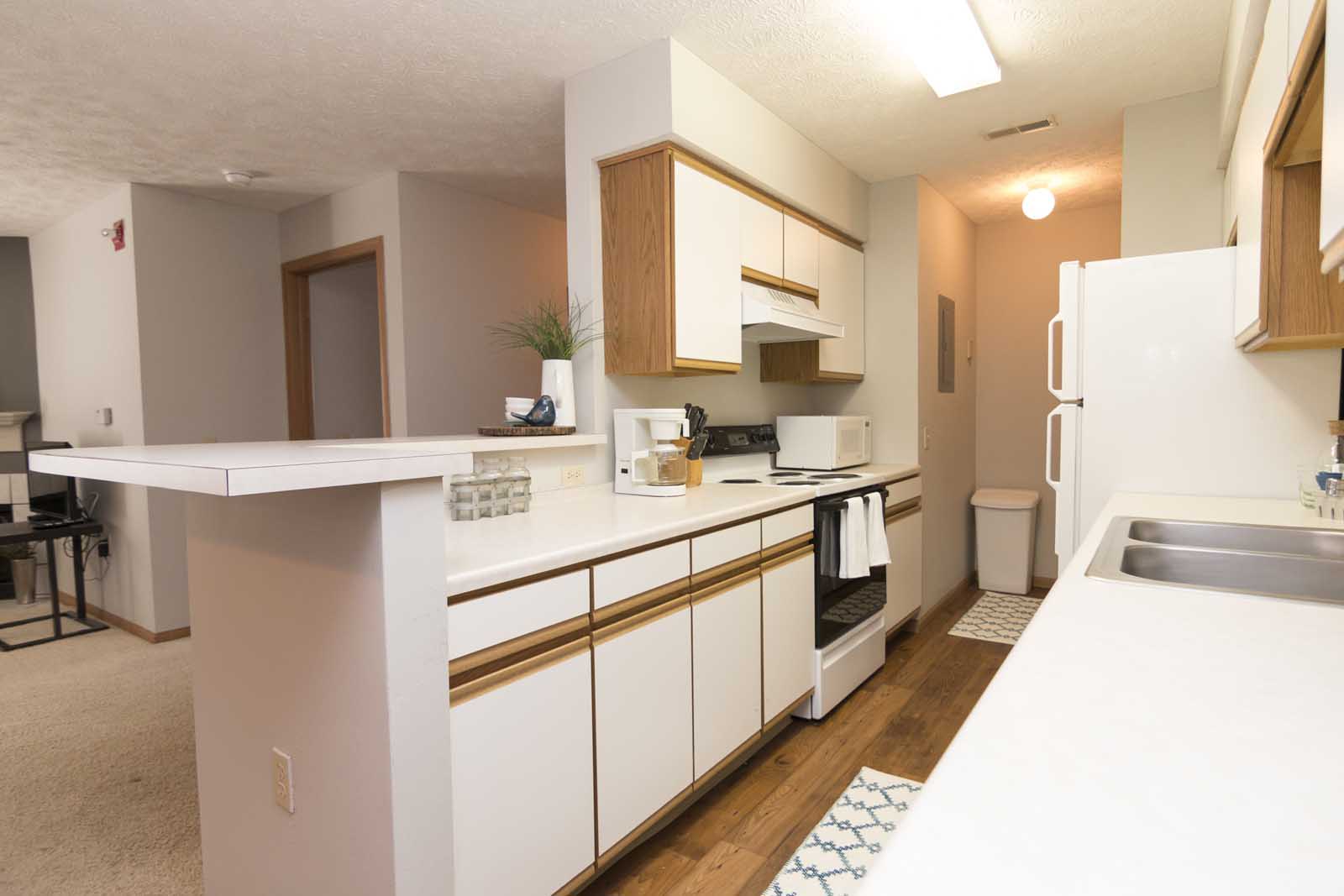 A traditional kitchen with a breakfast bar, white and oak cabinets, and white appliances.