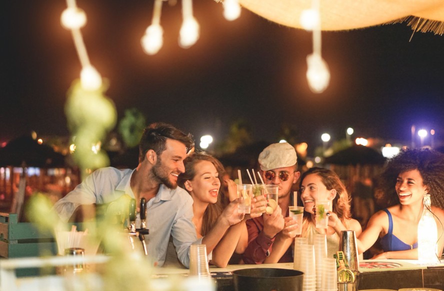 Friends laughing and toasting cocktails at nighttime rooftop bar with string lights