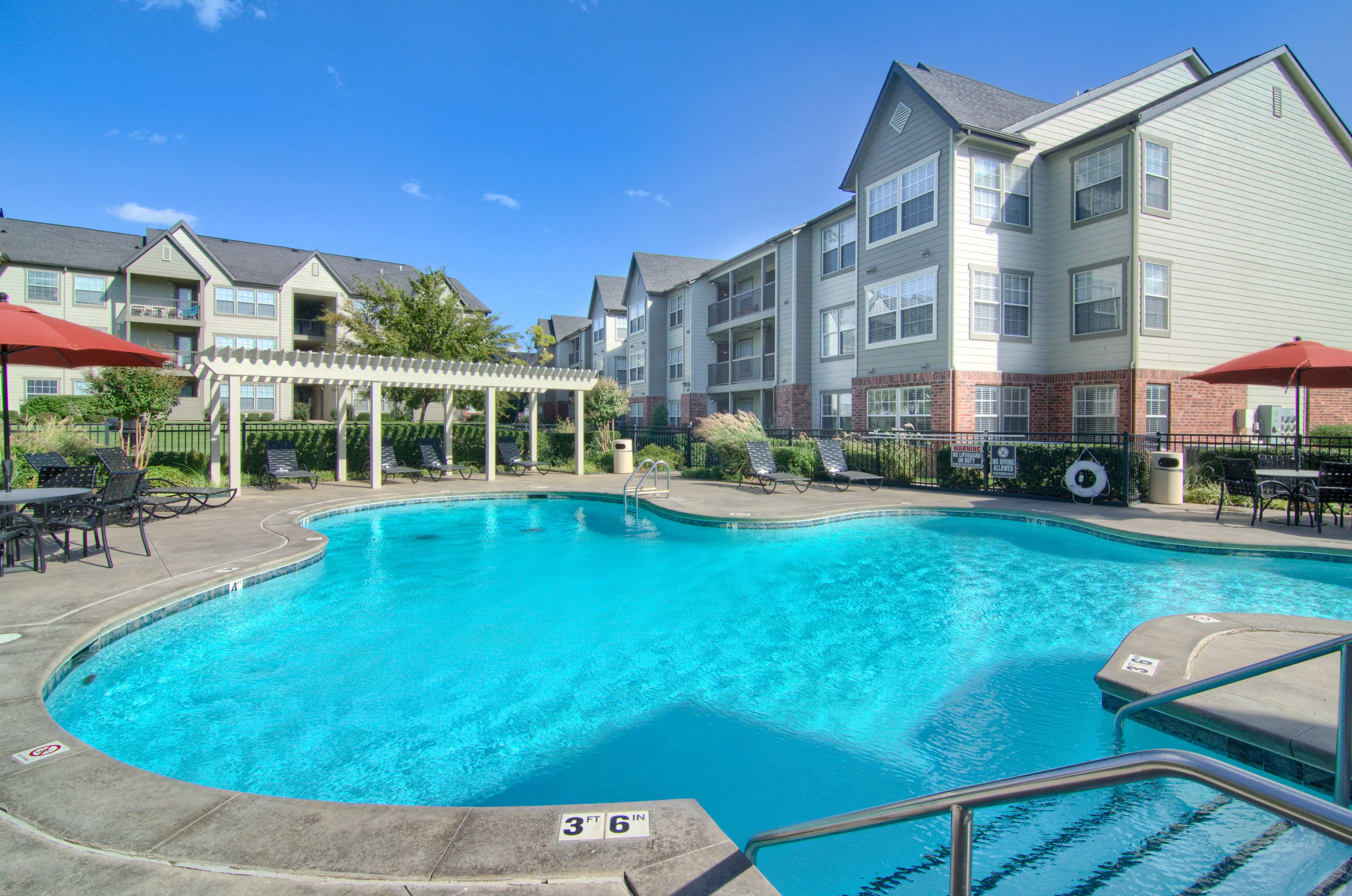 Large in-ground swimming pool with pool furniture and umbrellas at Villas at Preston Lake Apartment Homes in Owasso, OK.