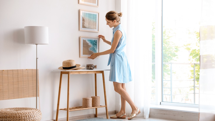 woman hanging wall art in her apartment living room