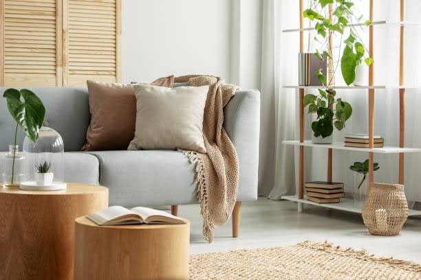 A cozy, bright living room in Atlanta, GA, features a gray sofa with velvet pillows, a knitted throw blanket, wood tables, and plants on a shelf.