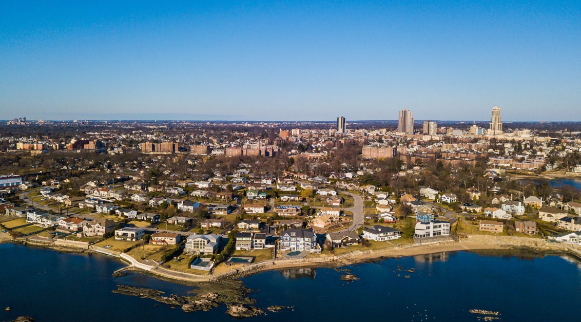 Aerial view of the Premium Point waterfront neighborhood in New Rochelle, New York, featuring luxury waterfront homes along Long Island Sound with the downtown New Rochelle skyline in the background.