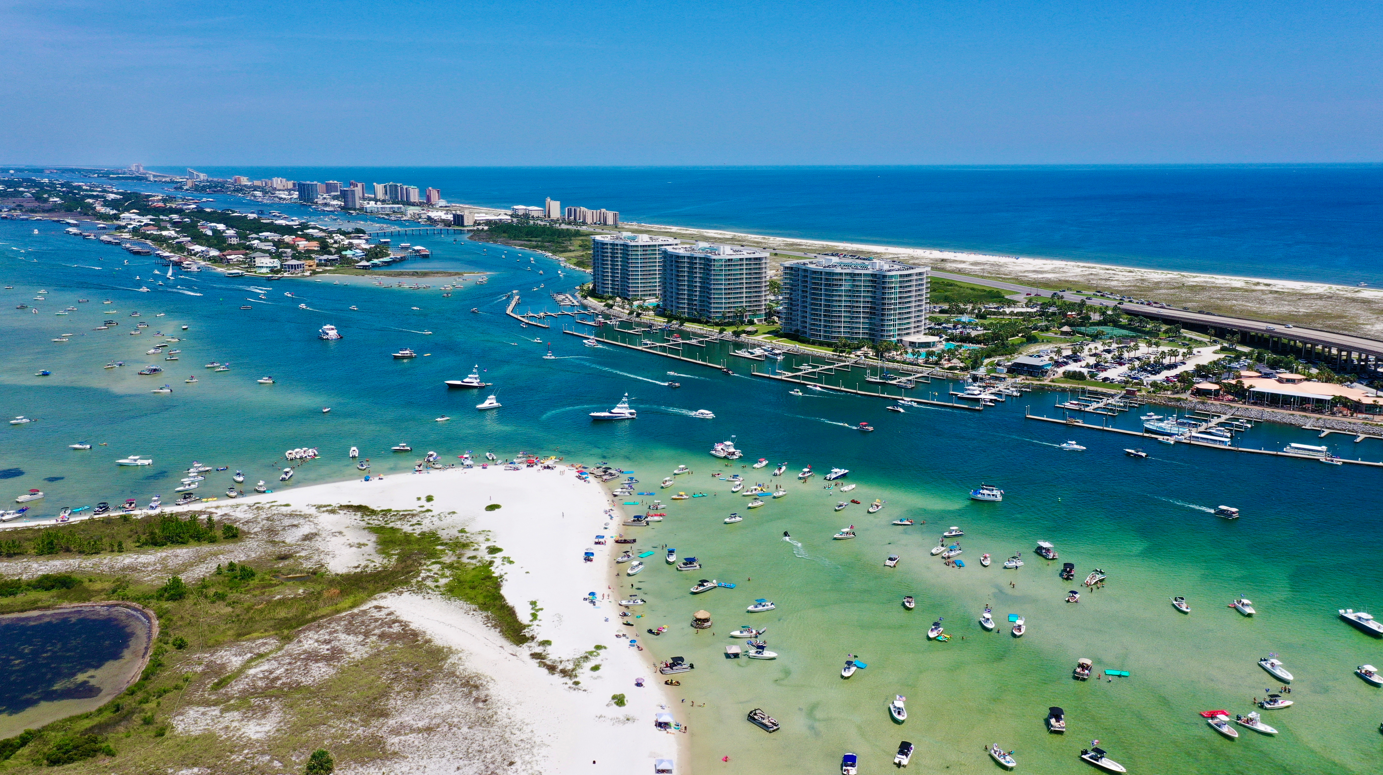 Aerial view of Orange Beach, Alabama coastline with boats, turquoise water, and waterfront condominiums near Perdido Pass.