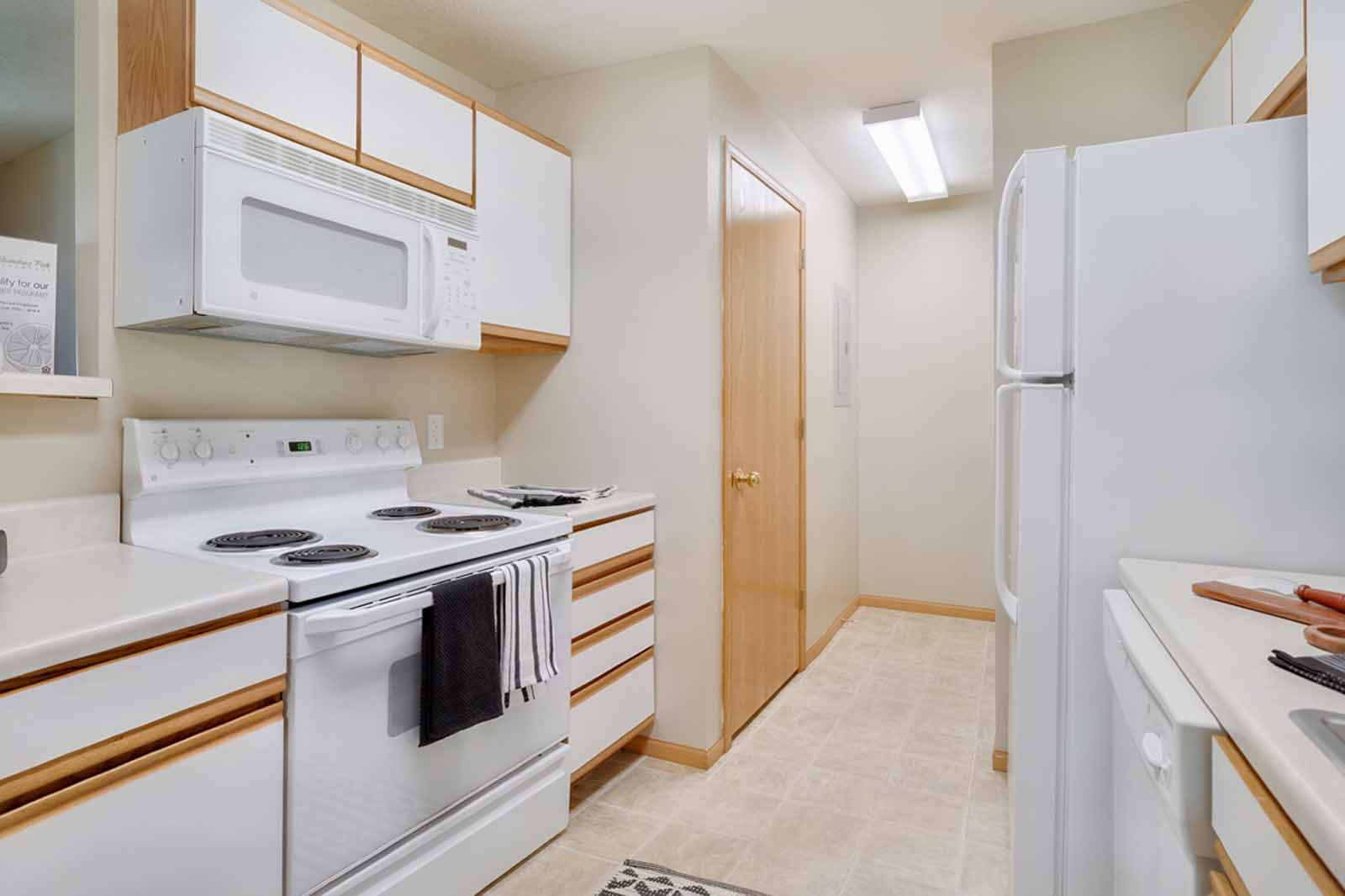 One side of a galley-style kitchen with upper and lower cabinets, stove, and built in microwave