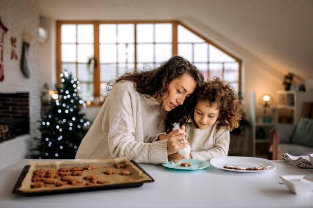 Mother and daughter decorate holiday cookies in their cozy Wesley Hampstead apartment living area with a lit holiday tree in the background.