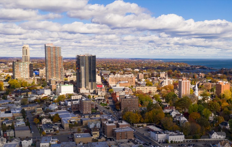 Aerial view of downtown New Rochelle with high-rise buildings and a scenic waterfront in the distance
