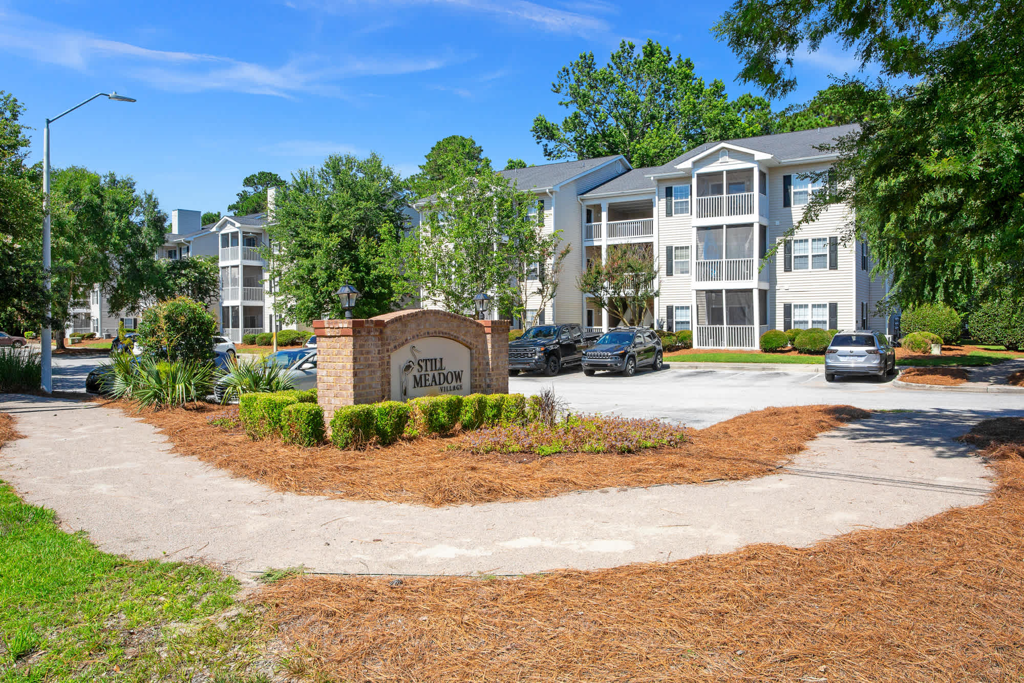 A scenic pathway lined with trees and shrubs leads to an apartment home in Still Meadow Village Apartments, Wilmington, NC.