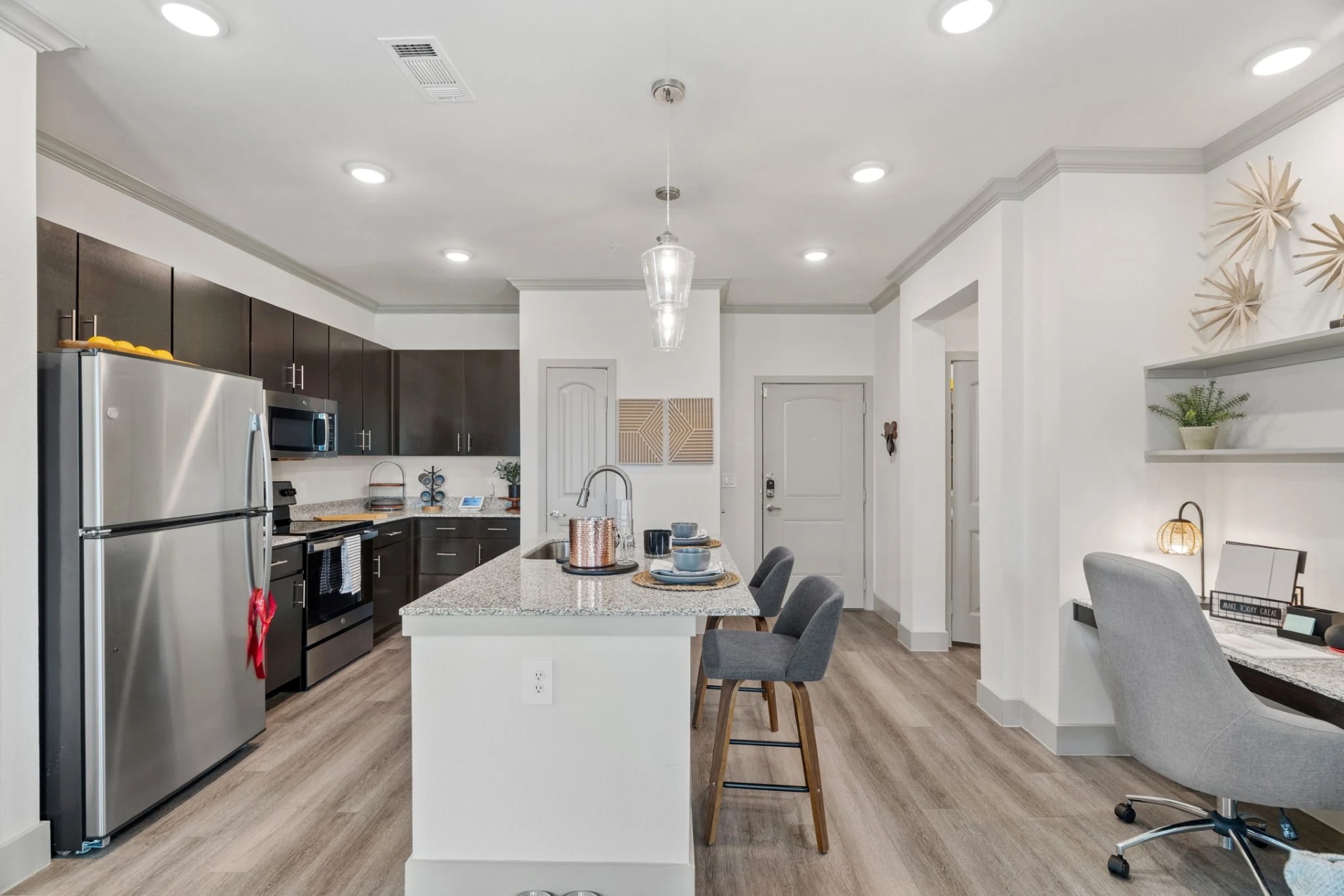 A kitchen featuring dark wood cabinets and a granite island resting near a wooden desk holding a grey chair.