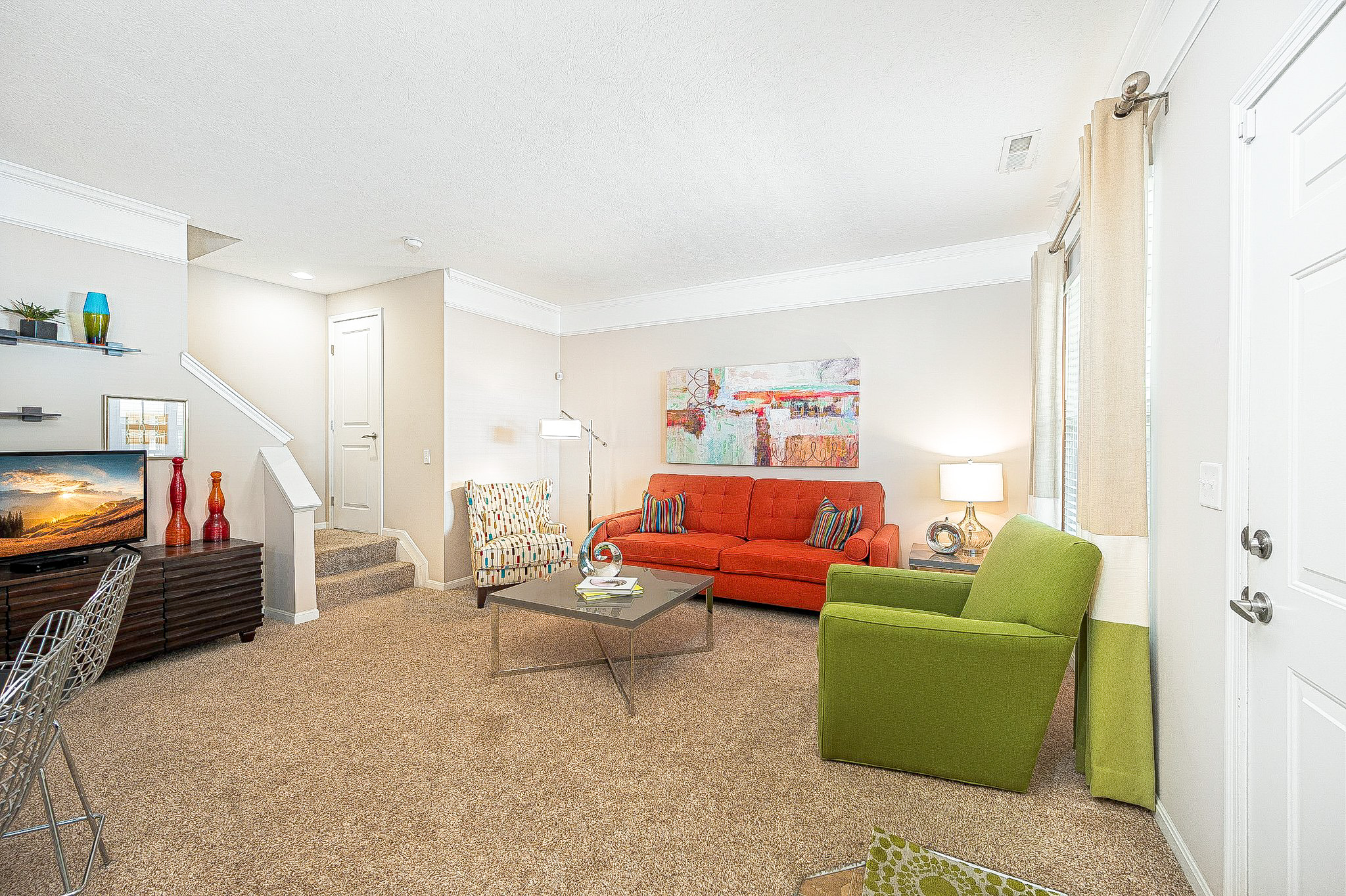 Bright living room inside a townhome at Albany Glen in New Albany, Ohio, featuring neutral walls, carpeted flooring, colorful furniture, and large windows with natural light.