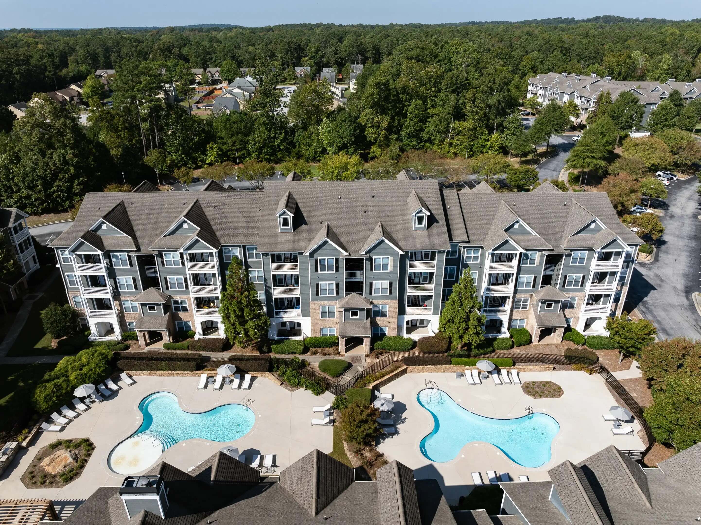 The large Wesley Kensington apartment building standing near two blue swimming pools bordering a green forest.